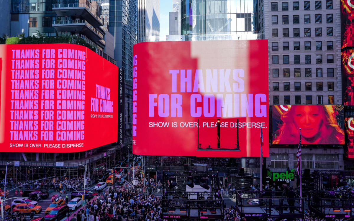 Times Square billboards in hot pink and red read THANKS FOR COMING. SHOW IS OVER. PLEASE DISPERSE., with a screen of Madonna's face to the right.